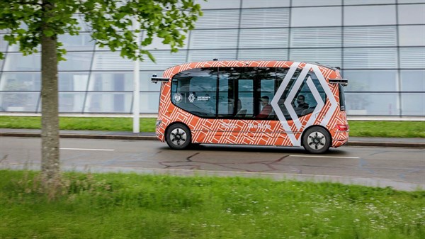 Autonomno vozilo u obliku minibusa vozi cestom uz zgradu, s prepoznatljivim geometrijskim uzorkom na karoseriji
