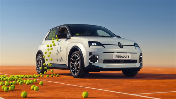 Vozilo Renault 5 E-Tech electric u bijeloj boji s teniskim lopticama koje se rasipaju uz vozilo na narančastoj teniskoj podlozi