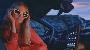 Žena s dugom plavom kosom i modernim sunčanim naočalama sjedi u unutrašnjosti vozila Renault, odjevena u narančastu košulju. U pozadini se vidi kameniti krajolik pri zalasku sunca, dok je u prvom planu moderan dodirni zaslon vozila.
