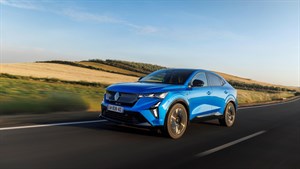 Plavi Renault Rafale vozi cestom kroz valoviti krajolik s poljima i šumarcima pod vedrim nebom.