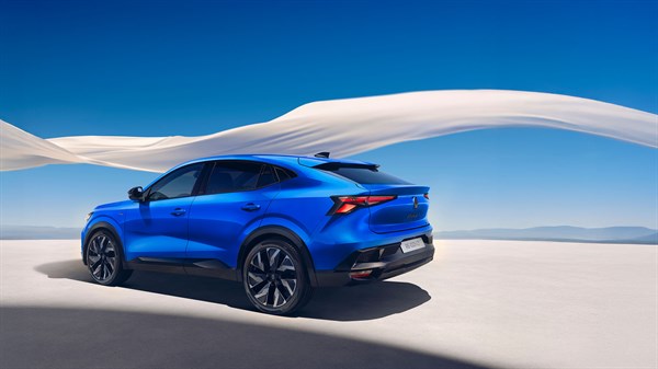 Bočni stražnji prikaz plavog SUV vozila u vožnji po svijetloj podlozi, s crnim naplatcima i istaknutim stražnjim svjetlima, na pozadini plavog neba i svijetlih dina.
