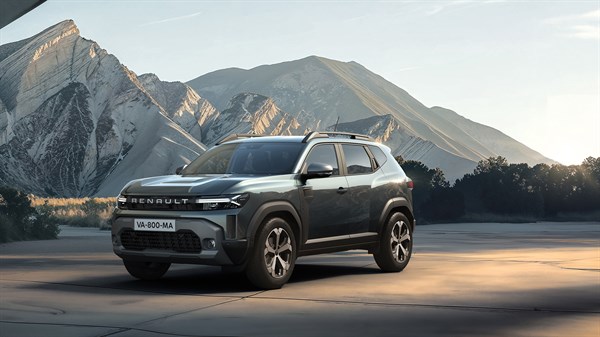 Sivo vozilo Dacia Duster parkirano na makadamskom putu s planinama u pozadini.