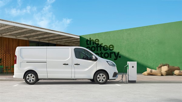 Bijelo vozilo Renault Trafic Van parkirano ispred moderne zgrade s natpisom "the coffee factory" i punjačem za električna vozila.