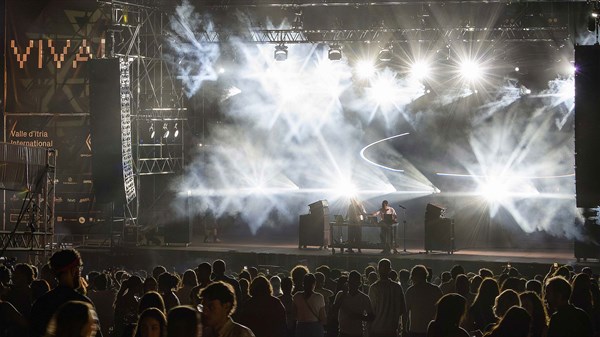 Glazbeni festival s velikom pozornicom, snažnim svjetlosnim efektima i publikom ispred pozornice tijekom večernjeg koncerta.