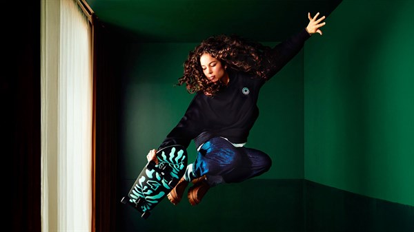 Osoba u pokretu u modernom interijeru s tamnozelenom pozadinom, kao dio lifestyle suradnje brenda.