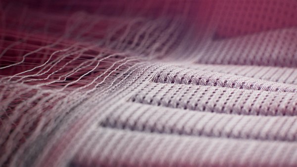 Makro prikaz tekstilne površine s vidljivom strukturom vlakana i uzorkom šavova u ružičastim i sivim tonovima.