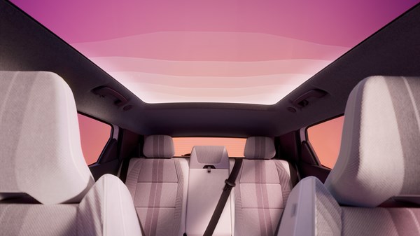 Unutrašnjost vozila Renault Scenic E-Tech electric s pogledom na stražnja sjedala i panoramski stakleni krov, u crveno-ružičastom osvjetljenju.
