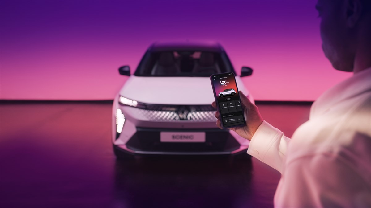 Osoba drži pametni telefon s aplikacijom dok je ispred nje parkirano vozilo Renault Scenic u osvijetljenom prostoru s ljubičastom pozadinom.







