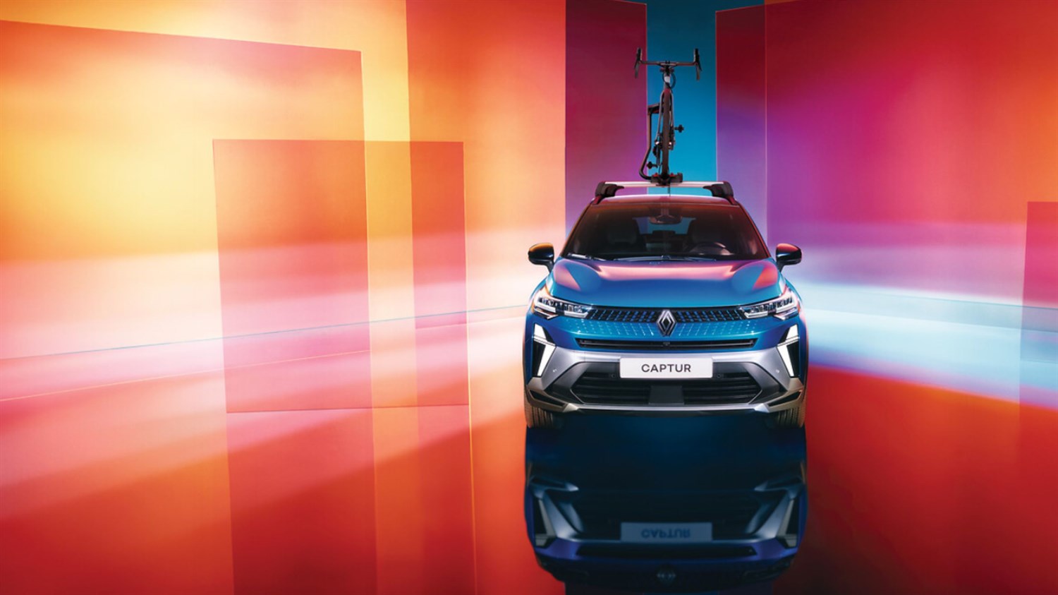 Renault Captur prikazan sprijeda, u živopisnom studiju s apstraktnom pozadinom u narančastim, ružičastim i plavim tonovima; na krovu vozila je pričvršćen bicikl.