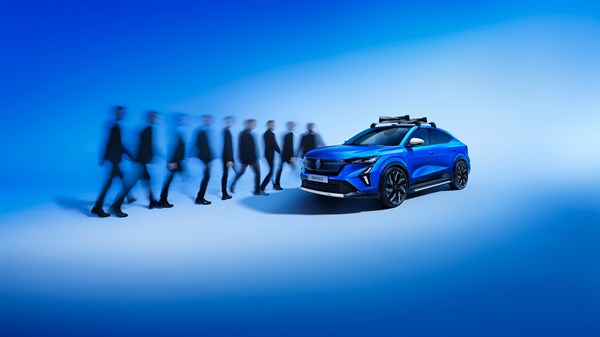 Plavi Renault Rafale E-Tech hybrid s krovnom torbom parkiran nasuprot grupi muškaraca u crnim odijelima u pokretu, na plavoj pozadini.