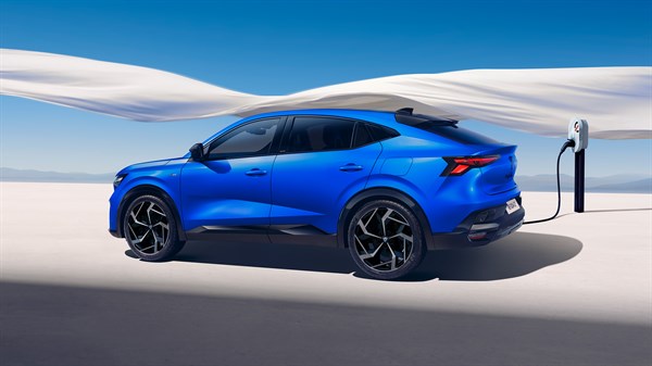 Vozilo Renault Rafale full hybrid E-Tech u plavoj boji povezano na punionicu, smješteno u minimalističkom bijelom krajoliku s tkaninom koja se vijori u pozadini.