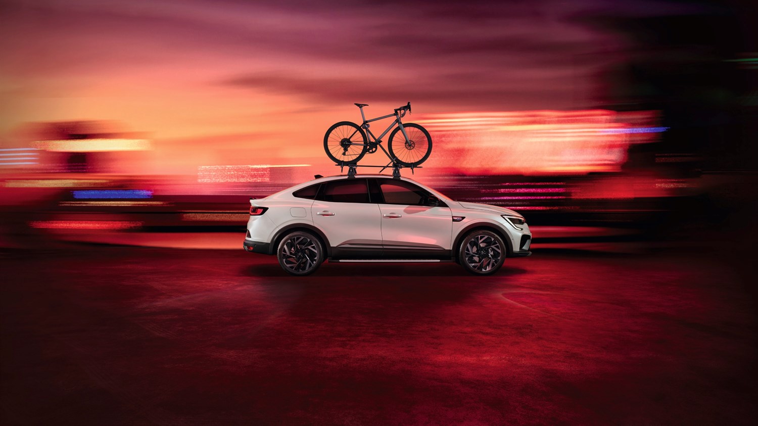Megane Conquest full hybrid E-Tech sa sportskim biciklom na krovu, parkiran u gradskoj zoni pri zalasku sunca.







