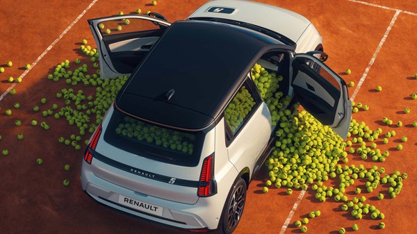 Vozilo Renault 5 E-Tech electric s otvorenim vratima i krovom okruženo teniskim lopticama na podlozi nalik terenu za tenis