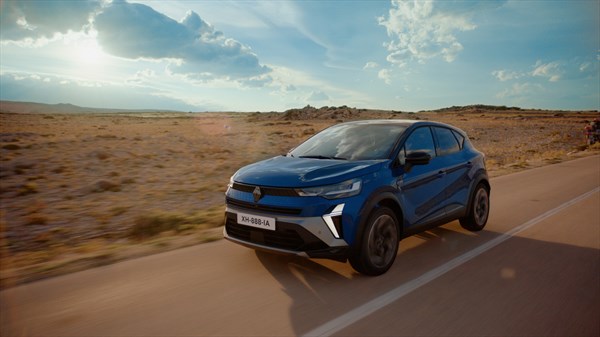 Captur full hybrid E-Tech u vožnji prirodnim krajolikom uz cestu, snimljen u pokretu s prednje strane u dinamičnoj kompoziciji.