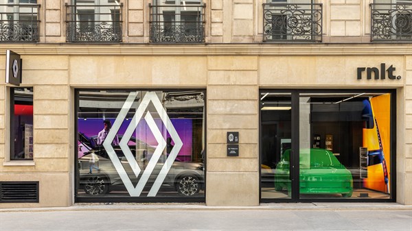 Izlog rnlt© showrooma s velikim Renault logotipom na staklu, kroz koji se vidi izloženo vozilo R5 Turbo 3E E-Tech electric, s naglašenim zelenim i narančastim refleksijama iznutra.







