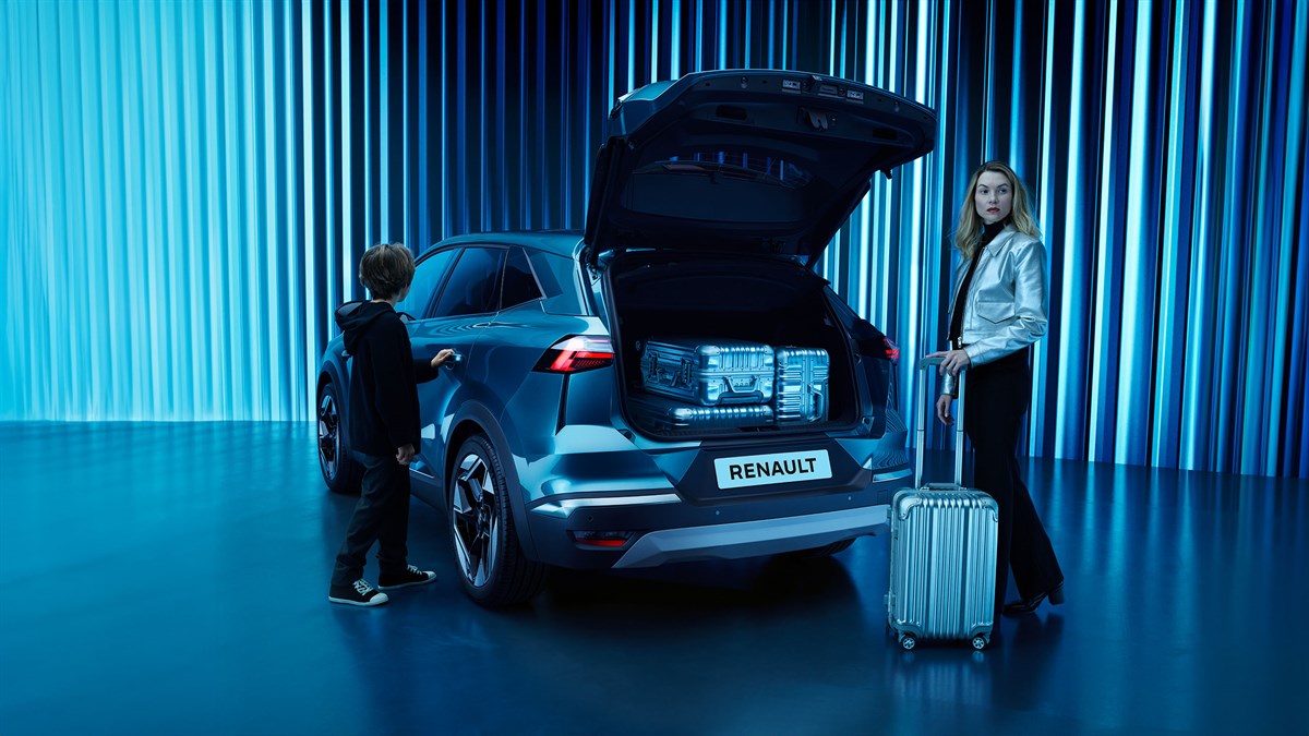 Renault Symbioz s otvorenim prtljažnikom, dječak dodiruje auto dok žena s koferom stoji pored njega.