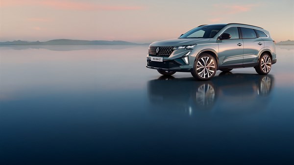 Vozilo Espace full hybrid E-Tech parkirano na ravnoj površini u zoru, s refleksijom na vodi i ružičastim nijansama neba u pozadini.