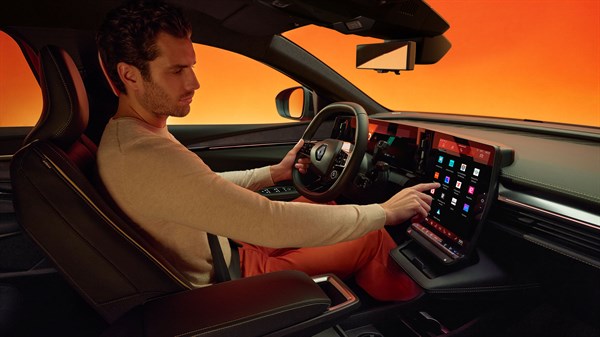 Vozač u unutrašnjosti Megane E-Tech electric koristi središnji zaslon osjetljiv na dodir dok sjedi u modernom, narančasto osvijetljenom interijeru.








