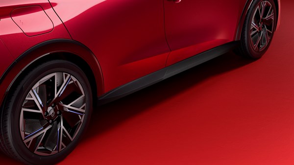 Bočni dio vozila Renault Clio snimljen u crvenom prostoru, s naglaskom na crne zaštite pragova i dizajn kotača.