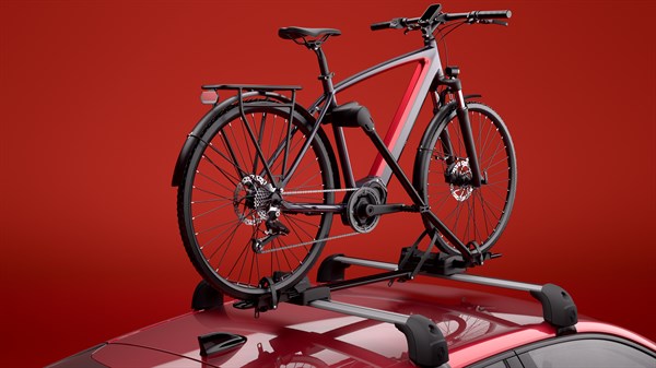 Bicikl postavljen na nosač za bicikle montiran na krovne nosače vozila Renault Clio, snimljeno u crvenom studijskom prostoru.