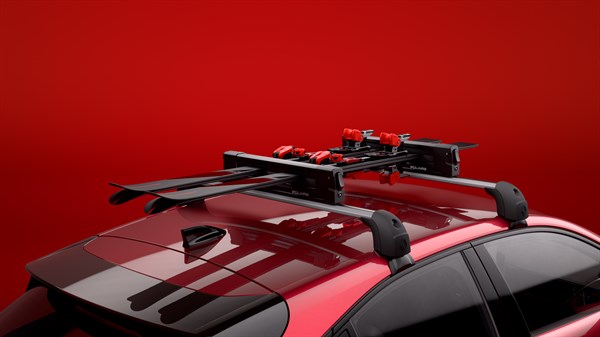 Nosači za skije montirani na poprečnim krovnim nosačima vozila Renault Clio, prikazani u crvenom ambijentu.