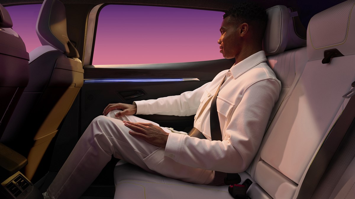 Putnik sjedi na stražnjem sjedalu u vozilu Renault, u svijetloj unutrašnjosti s velikim bočnim prozorom i pogledom na nebo u toplim večernjim tonovima.