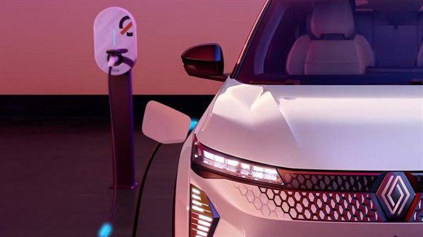 Prednji dio bijelog Renault Scenic E-Tech electric vozila spojenog na punionicu, snimljen u ambijentu toplih ružičastih i ljubičastih tonova.