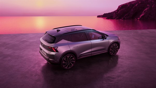 Renault Scenic u stražnjem tričetvrtinskom pogledu na mokroj obalnoj površini pri zalasku sunca, s ružičastim nebom, morem i stijenama u pozadini.