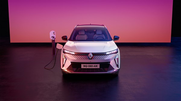 Bijelo vozilo Renault Scenic E-Tech electric sprijeda, parkirano u studiju s rozo-ljubičastom pozadinom, spojeno na punjač s lijeve strane.