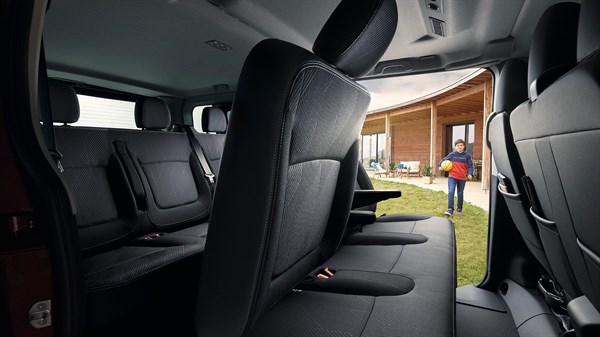 Unutrašnjost vozila s pogledom na stražnja sjedala, a kroz otvorena vrata u pozadini se vidi osoba ispred kuće.