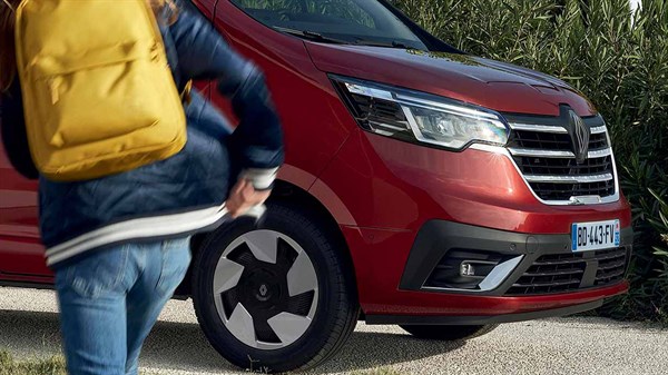 Prednji dio crvenog dostavnog vozila Renault s vidljivim svjetlom, maskom i 43 cm (17'') naplatcima; ispred vozila osoba u pokretu s žutim ruksakom.
