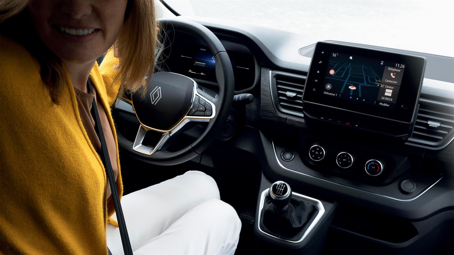 Vozačica sjedi za volanom vozila Renault Trafic Passenger; prikazan je moderan upravljač, ručni mjenjač i središnji zaslon na dodir s navigacijom. Unutrašnjost je dizajnirana funkcionalno i suvremeno.

