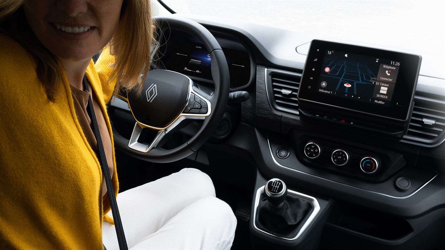 Vozačica sjedi za volanom vozila Renault Trafic Passenger; prikazan je moderan upravljač, ručni mjenjač i središnji zaslon na dodir s navigacijom. Unutrašnjost je dizajnirana funkcionalno i suvremeno.

