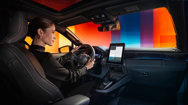 Vozačica u unutrašnjosti vozila Captur full hybrid E-Tech upravlja volanom ispred digitalnog zaslona u ambijentu s raznobojnim pozadinskim osvjetljenjem.