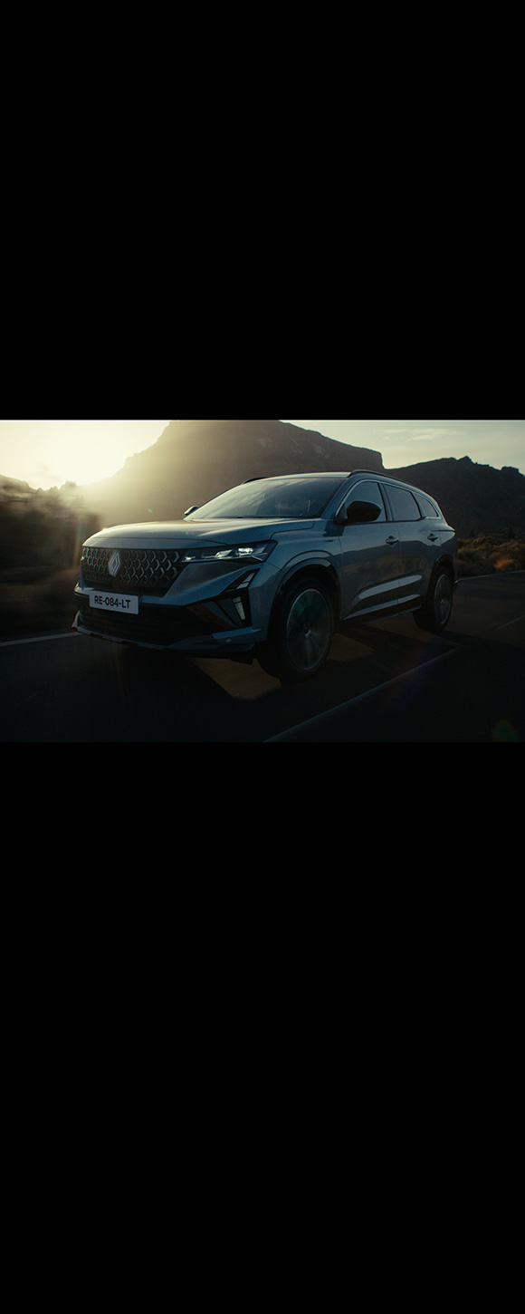 Vozilo Espace full hybrid E-Tech prikazano s prednje desne strane na reflektirajućoj površini uz zalazak sunca.