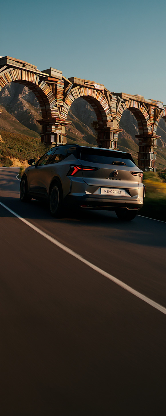 Renault Scenic vozi zavojitom planinskom cestom, snimljen straga, u prirodnom planinskom krajoliku.