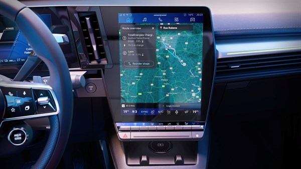 Unutrašnjost vozila Renault Scenic sa središnjim zaslonom koji prikazuje kartu navigacije i informacije o ruti, uključujući potrebna zaustavljanja radi punjenja.