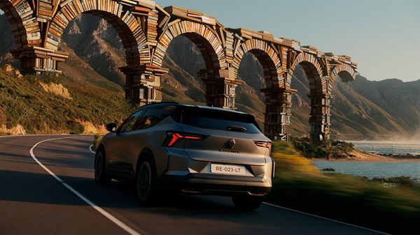 Renault Scenic snimljen straga tijekom vožnje uz obalu, ispod kamenog vijadukta u planinskom krajoliku.