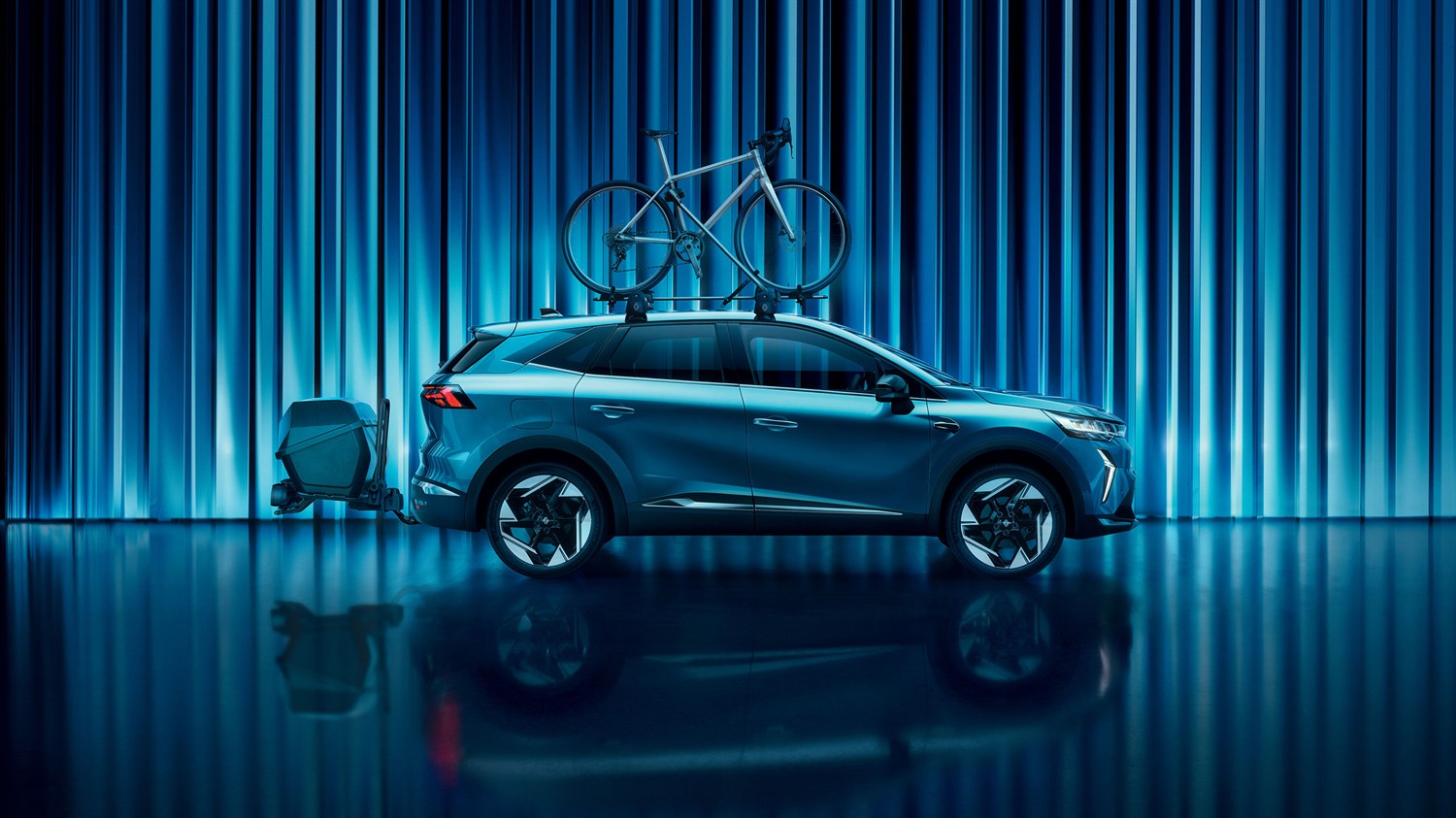 Plavi Symbioz, bočni pogled, s biciklom na krovnom nosaču i prtljagom straga, u studiju s plavim osvjetljenjem.