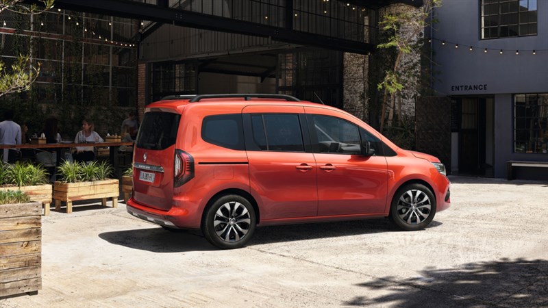 Narančasto vozilo Kangoo Passenger parkirano ispred modernog restorana s terasom i zelenilom.