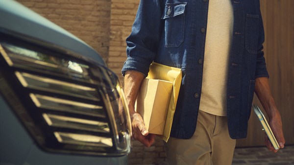 Osoba pored automobila nosi paket i dokumente.