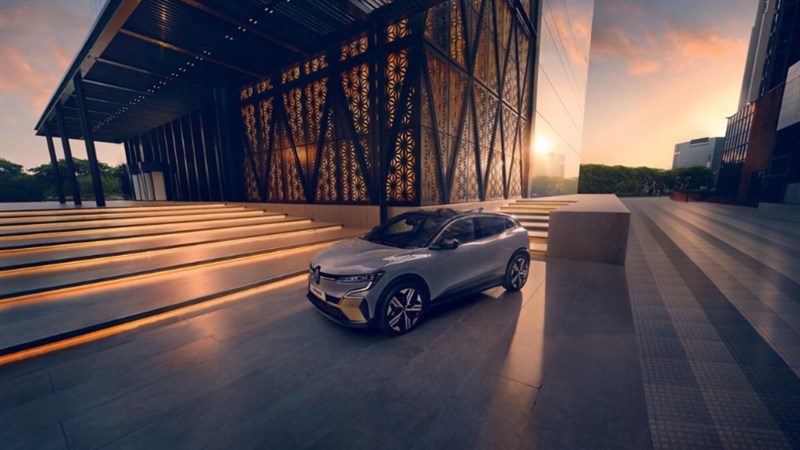 Dvije žene u živopisnoj odjeći stoje ispred plavog vozila Renault Captur ispred zgrade s neonskim znakom.