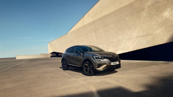 Žena naslonjena na plavo vozilo Renault Captur parkirano uz ogradu, u pozadini zalazak sunca.